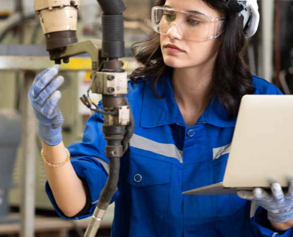 a woman wearing safety goggles and a blue shirt and holding a laptop