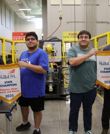 The four winners stand next to each other holding up their winner banners from SkillsUSA. A robot sits in the background.