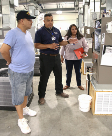 Michelle Espinosa (right), a TSTC admissions advisor at the Harlingen campus, takes U.S. Army veteran Abel Rodriguez (left) on a tour of TSTC’s HVAC Technology program, while HVAC instructor Jose Flores explains an example of the hands-on training that Rodriguez can expect.