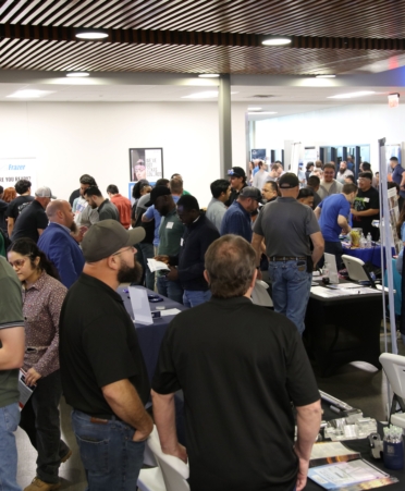 Students and employers gather around tables and chat with each other at a job fair.