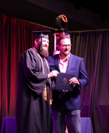 Moxley, wearing cap and gown, receives his diploma from Bryan Bowling, wearing a suit.