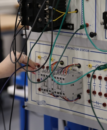 A panel is being operated by a student. Only her hand is shown. She wears a ring and a watch.