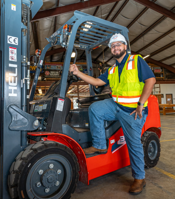 a man in a safety vest and white helmet sitting on a forklift