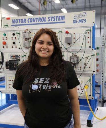 Vanesa Medrano stands wearing a black t-shirt with industrial systems lab equipment in the background