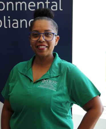 Andrea poses while wearing a green TSTC shirt. A sign for the OSEC program is behind her
