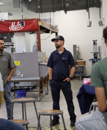 Representatives from Coolers inc stand in front of students one wearing a grey shirt, the other, a blue shirt and hat.