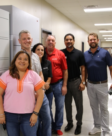Six people stand in a row in front of the new food lockers, all posing for the camera.