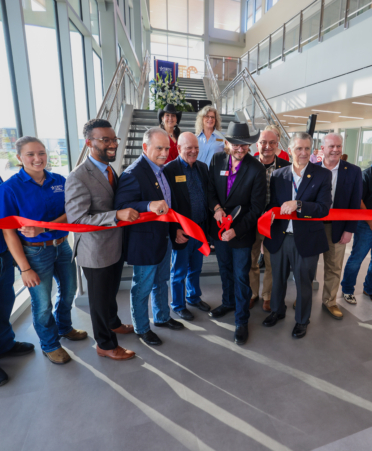 Officials stand in a line as Bryan Bowling, wearing a cowboy hat, cuts the red ribbon in front of them.