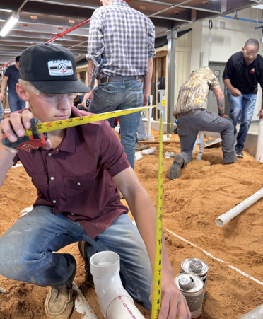 Plumbing student using tape measure in sand box