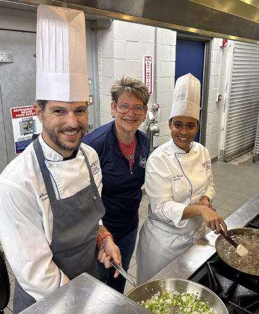 two chefs and lady in blue shirt in a commercial kitchen