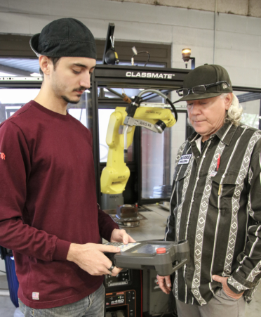 Texas State Technical College Welding instructor Kenneth Moore (right) guides student Andrew Maciel through programming an automated welding robotic arm during a lab at TSTC’sHarlingen campus.