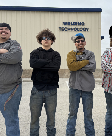 four welders standing in front of the shop